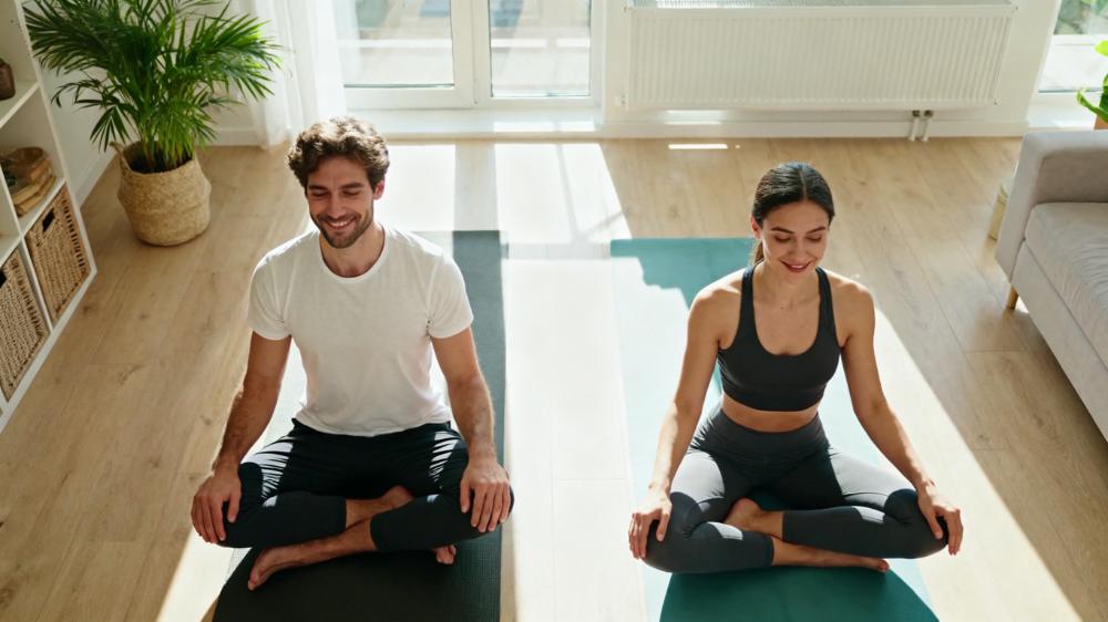 A couple practicing yoga together in a sunlit room, representing the trend of holistic wellness to build intimacy 2025.