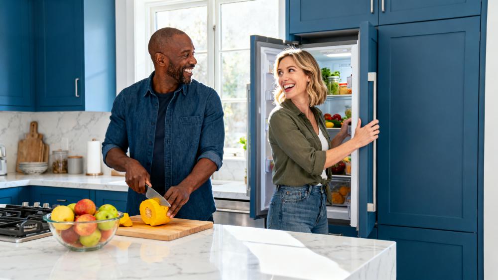 A happy couple laughing together while cooking in the kitchen, demonstrating a key daily intimacy how to strategy of creating shared experiences.