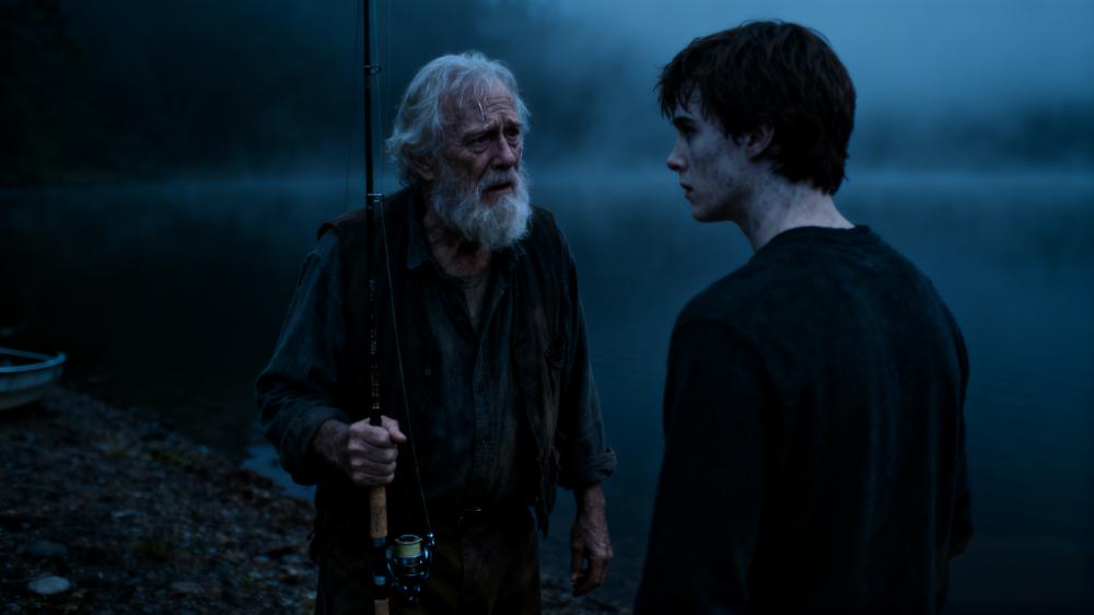 An old fisherman speaking to a distraught Ethan by a dark lake shore, revealing a haunting secret after a first love confession.