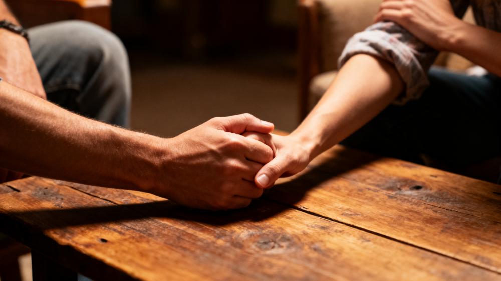 A close-up of a couple holding hands across a table, a key practice in learning how to improve intimacy through vulnerability.